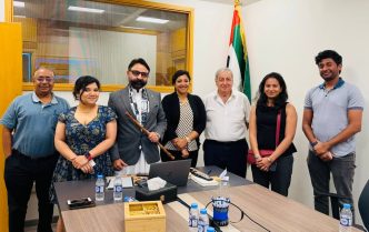 Group of seven professionals posing for a photo in a conference room with an Indian flag in the background.
