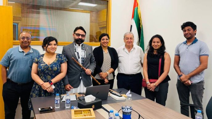 Group of seven professionals posing for a photo in a conference room with an Indian flag in the background.