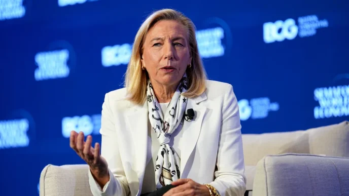 Panelist in a white blazer speaks on stage, gesturing with her left hand against a blue conference backdrop.