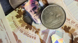 Close-up of Canadian currency: coins on top of colorful banknotes, including a large silver dollar and a 100-dollar note.