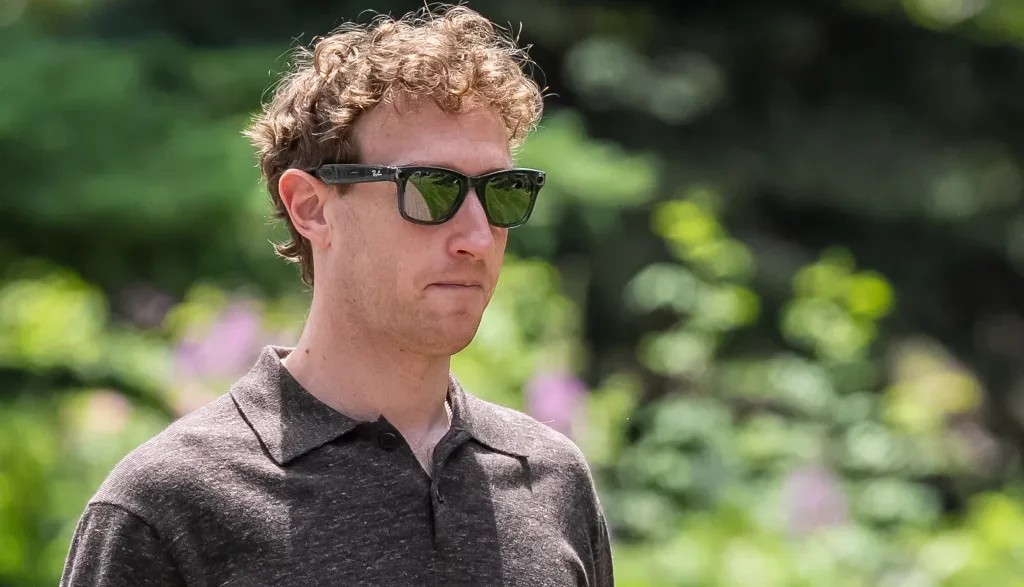 Man wearing dark sunglasses and a dark polo shirt, standing in a sunny garden.