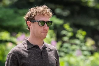 Man wearing dark sunglasses and a dark polo shirt, standing in a sunny garden.