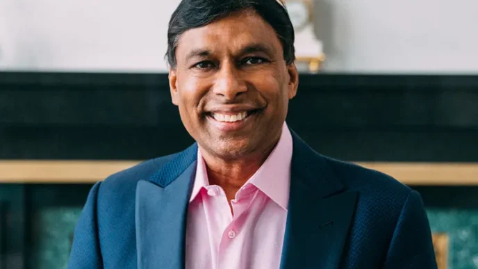 Smiling man in a pink dress shirt and blue blazer posing for a portrait.