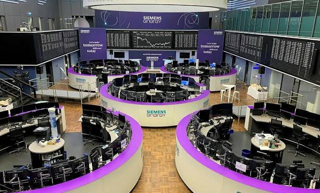 Modern trading floor with curved purple desks, numerous computer terminals, and large Siemens Energy display boards.
