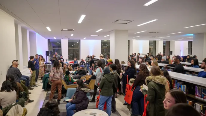 Crowded library room with people standing and sitting around, a panel at the front addressing the audience.
