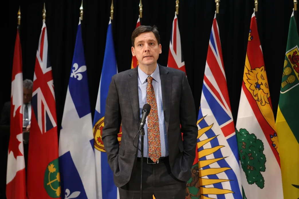 British Columbia Premier David Eby speaking at a press conference with provincial flags behind him