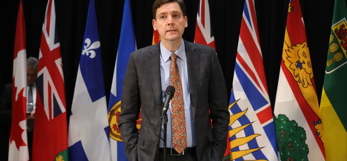 British Columbia Premier David Eby speaking at a press conference with provincial flags behind him