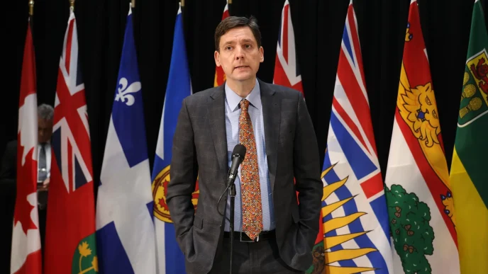 British Columbia Premier David Eby speaking at a press conference with provincial flags behind him