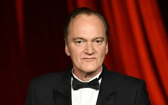 Quentin Tarantino in a tuxedo against a red curtain backdrop