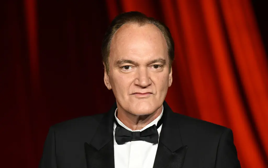 Quentin Tarantino in a tuxedo against a red curtain backdrop