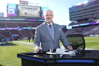 Rich Eisen standing at a broadcast desk inside a football stadium