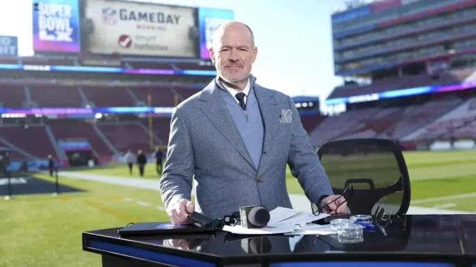 Rich Eisen standing at a broadcast desk inside a football stadium